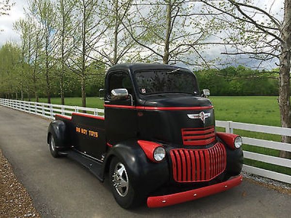 an old black and red truck parked on the side of a road next to a white fence