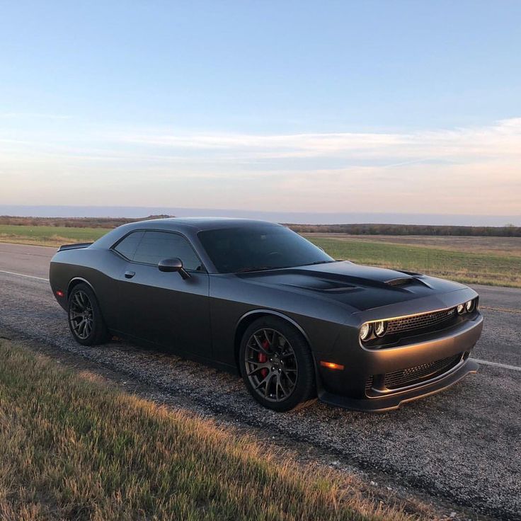 a black car is parked on the side of the road in front of an open field