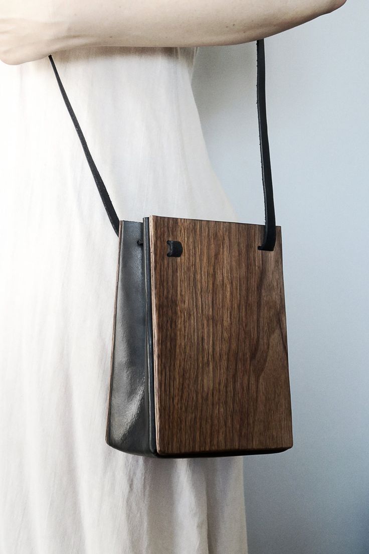 a wooden bag hanging from the back of a white shirt with a black leather strap