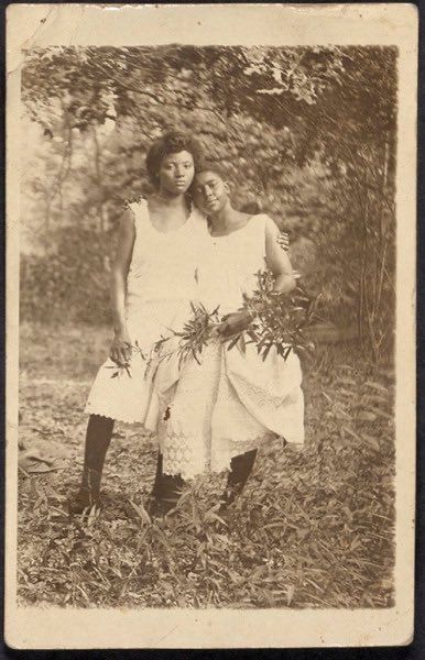 an old black and white photo of two women standing in the grass, one holding flowers