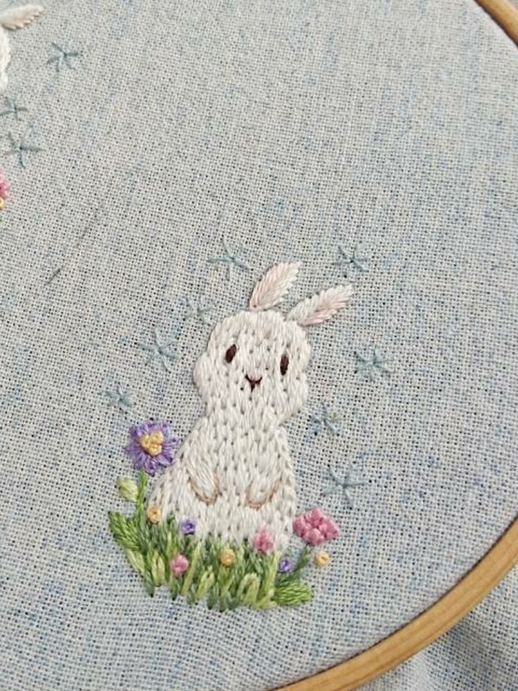 a close up of a cross stitch bunny on a blue background with flowers and stars