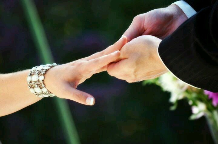 a close up of two people holding hands with flowers in the background