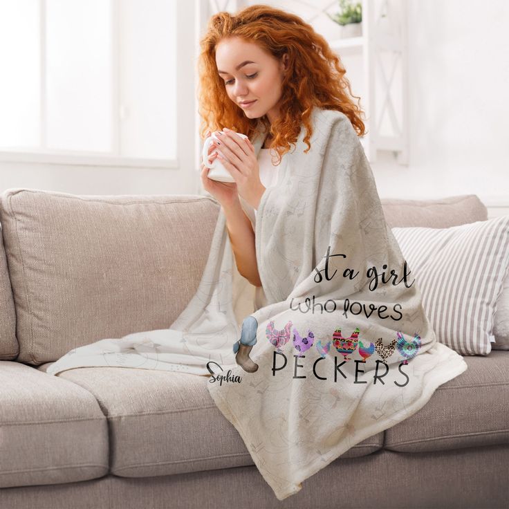 a woman wrapped in a blanket sitting on top of a couch holding a coffee cup