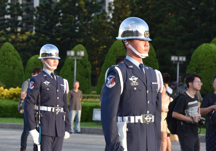 two men in uniform standing next to each other with helmets on their heads and people walking by