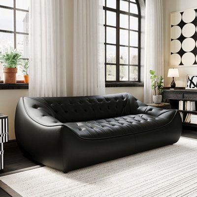 a black leather couch sitting in front of a window next to a table and chair