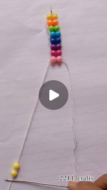 a person is holding a string with beads on it and making a rainbow bead necklace