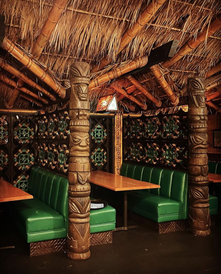 the inside of a restaurant with green leather seats and tiki style wood tables, that are covered by straw roofing