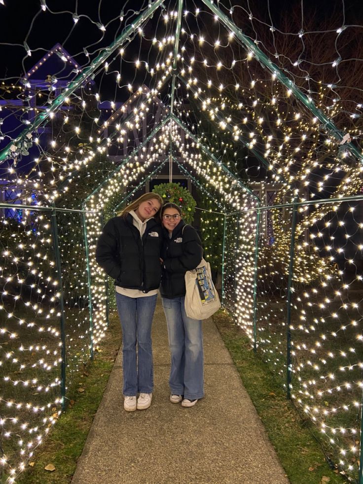 two women standing in front of a lit up gazebo at night with christmas lights all around them