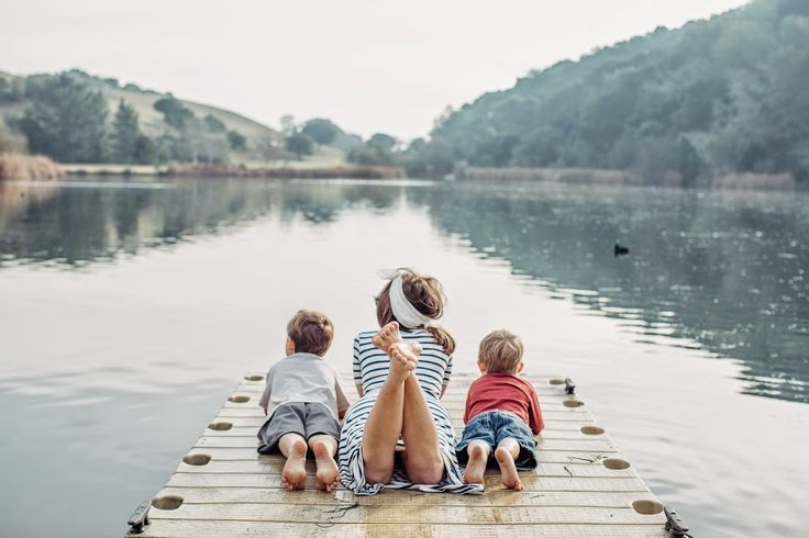 three children sitting on a dock looking out at the water