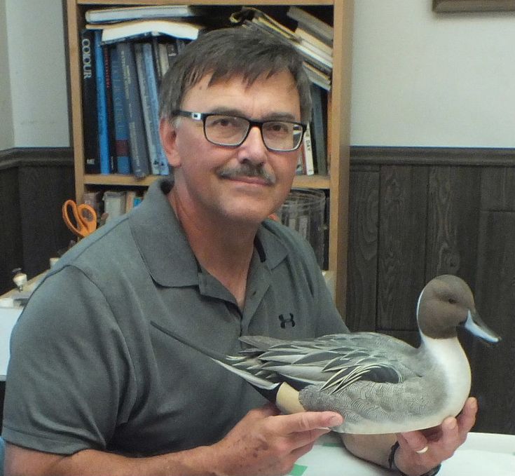 a man sitting at a table with a duck in his hand and books on the shelves behind him