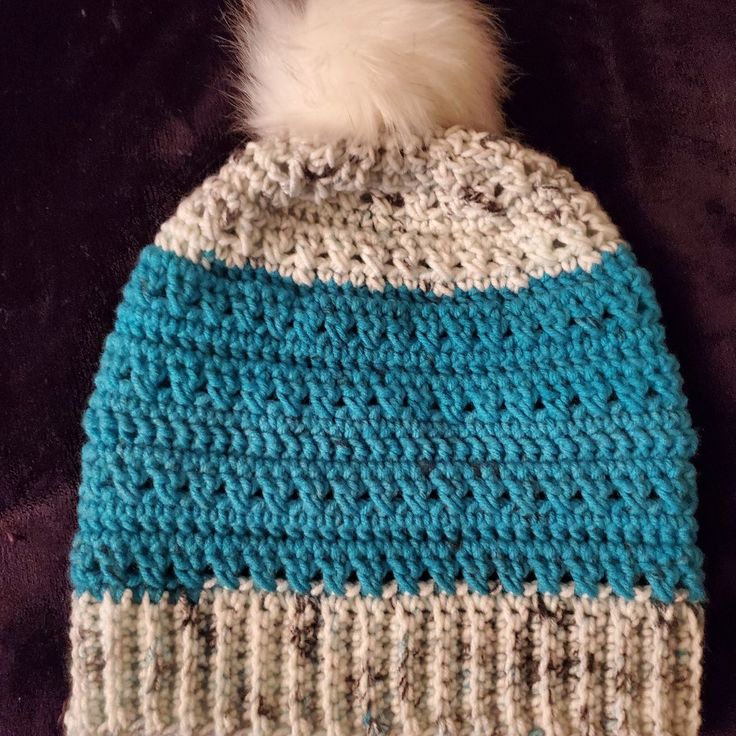 a blue and white knitted hat with a fur pom