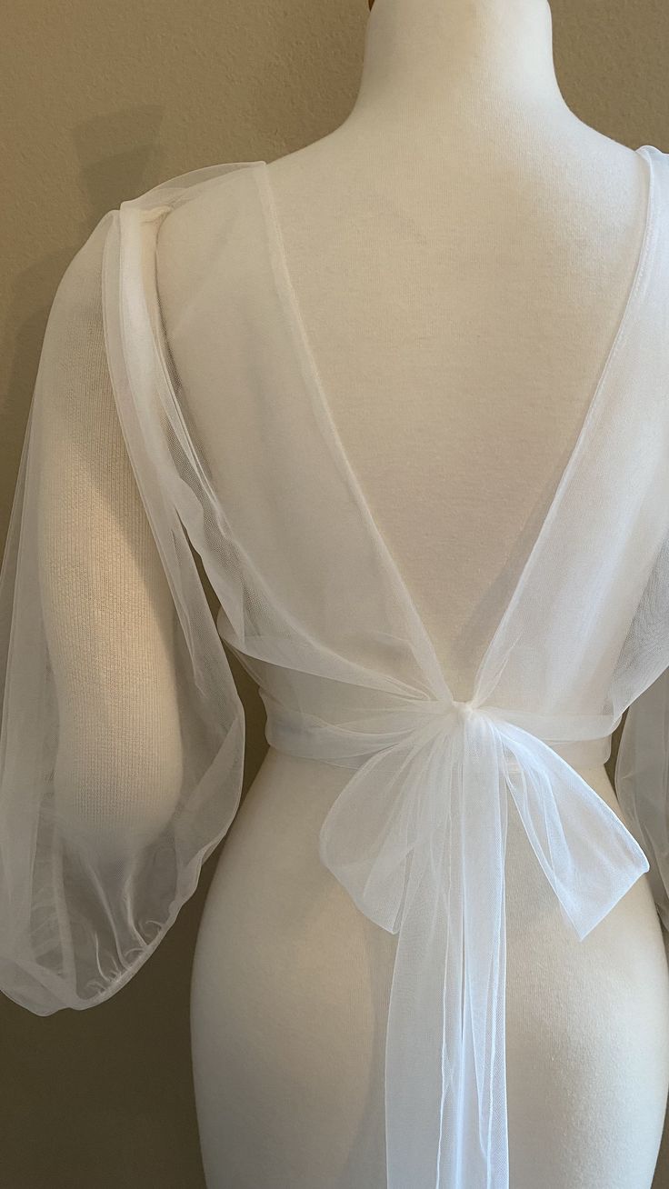 the back of a white dress with sheer sleeves and a bow at the waistline