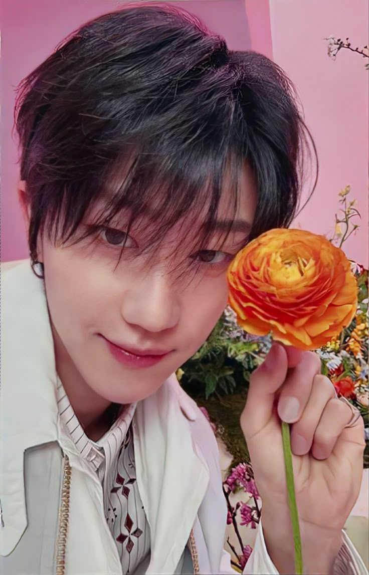 a young man holding an orange flower in front of his face