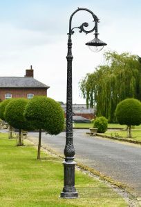 an old fashioned lamp post in the middle of a grassy area next to a road