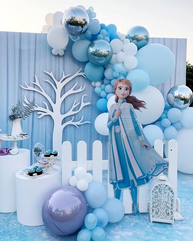 a blue and white backdrop with balloons, trees, and a princess standing in front of it