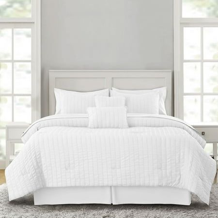 a bed with white comforter and pillows in front of two large window panes