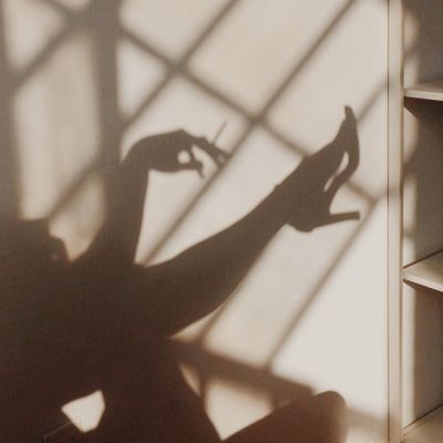 the shadow of a woman sitting in a chair with her arm up against a bookshelf