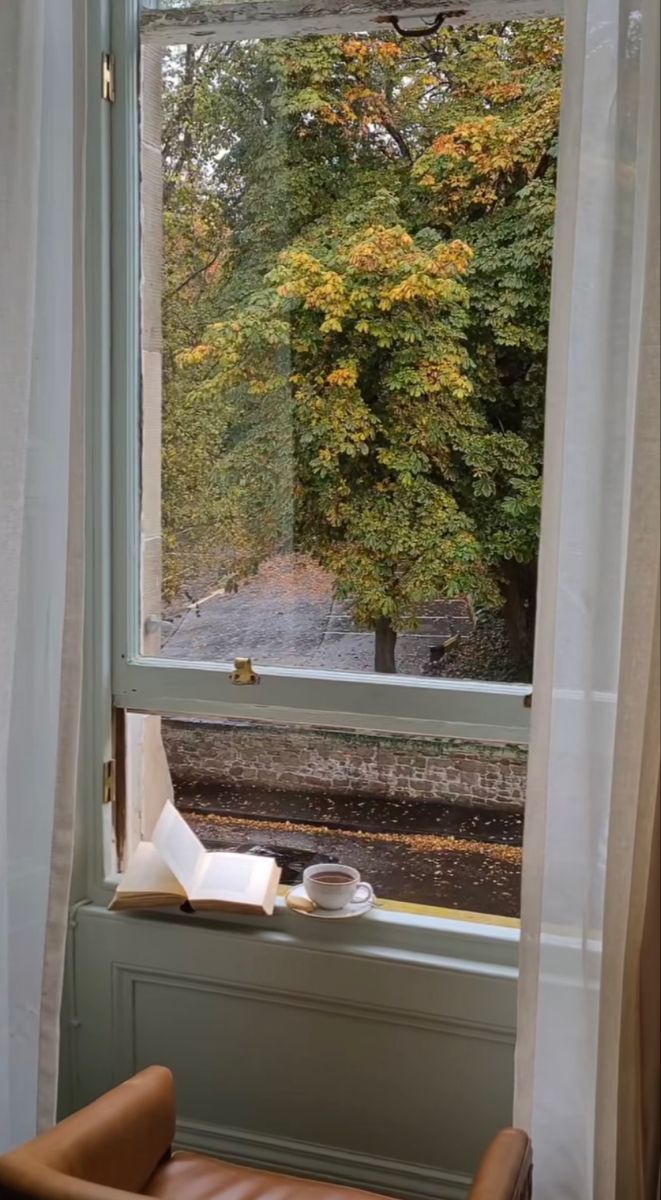 a chair sitting in front of a window next to a book and cup on top of a table