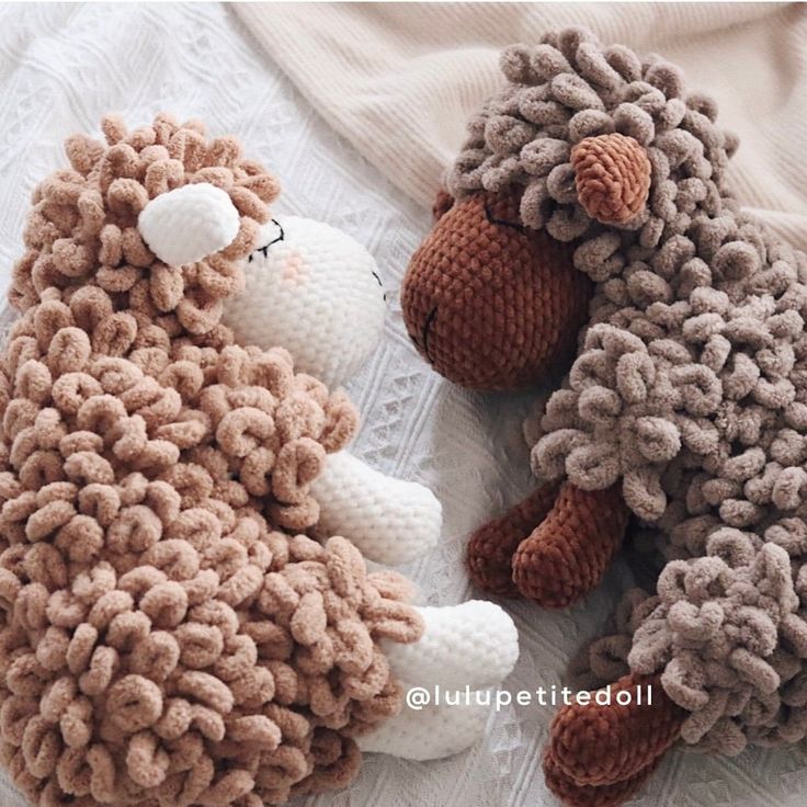 two knitted sheep laying next to each other on a white blanket with the same pattern