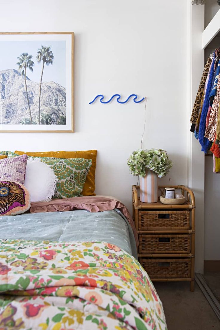 a bed with colorful sheets and pillows next to a painting on the wall above it