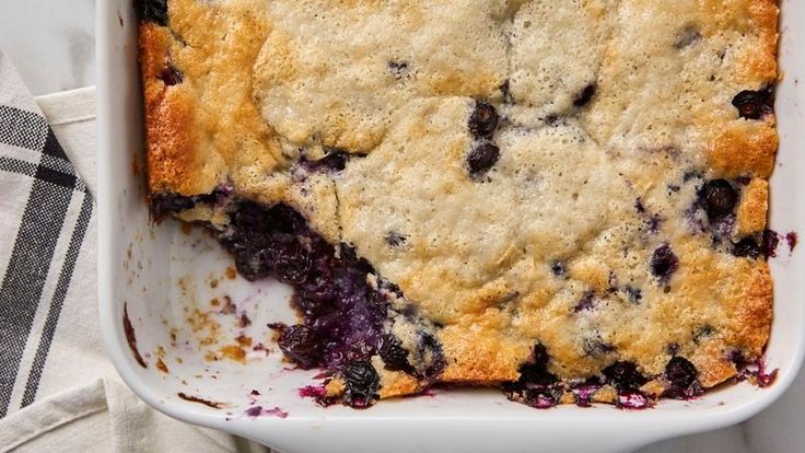 a casserole dish with blueberries in it on a white cloth next to a fork