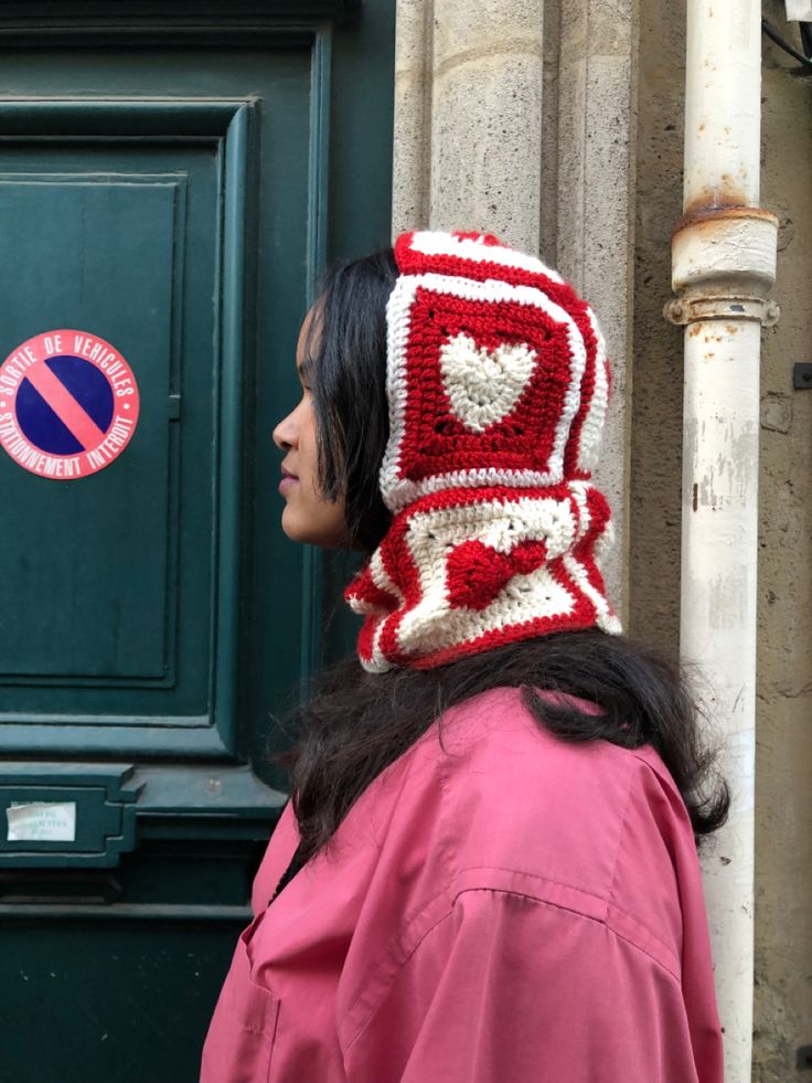 a woman standing in front of a green door wearing a red and white crocheted hat