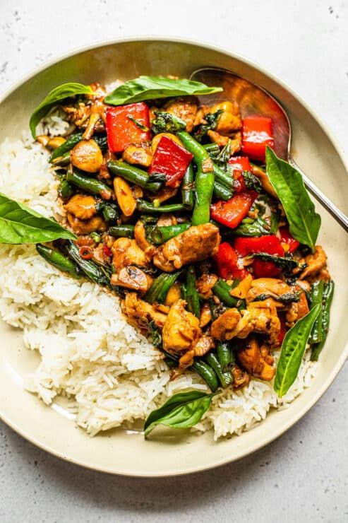 a white plate topped with chicken and vegetables on top of rice next to a fork