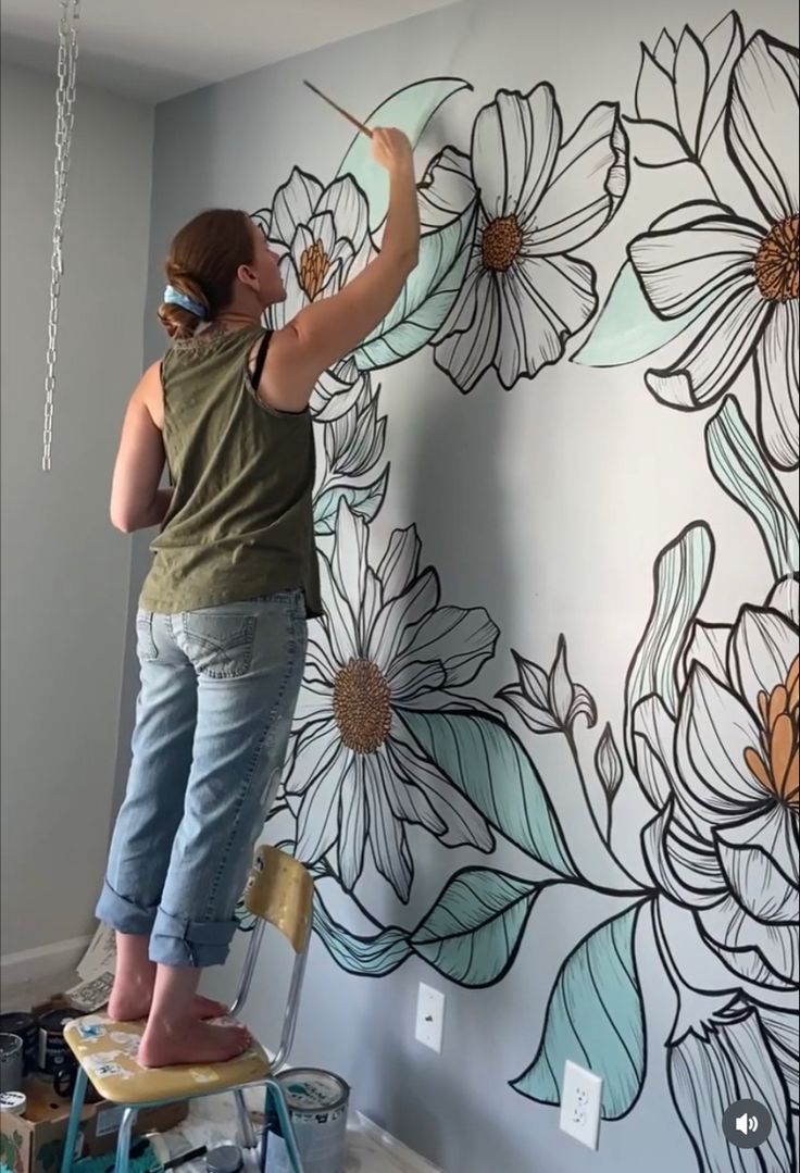 a woman is painting flowers on the wall