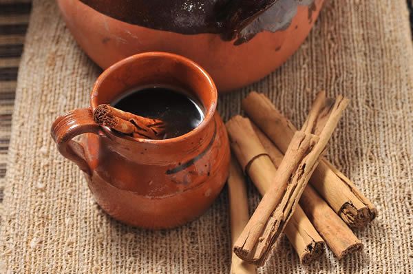 some cinnamon sticks and a cup of coffee on a table with an old pot in the background