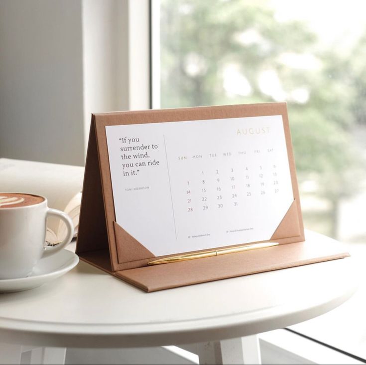 a desk calendar sitting on top of a table next to a cup of espresso