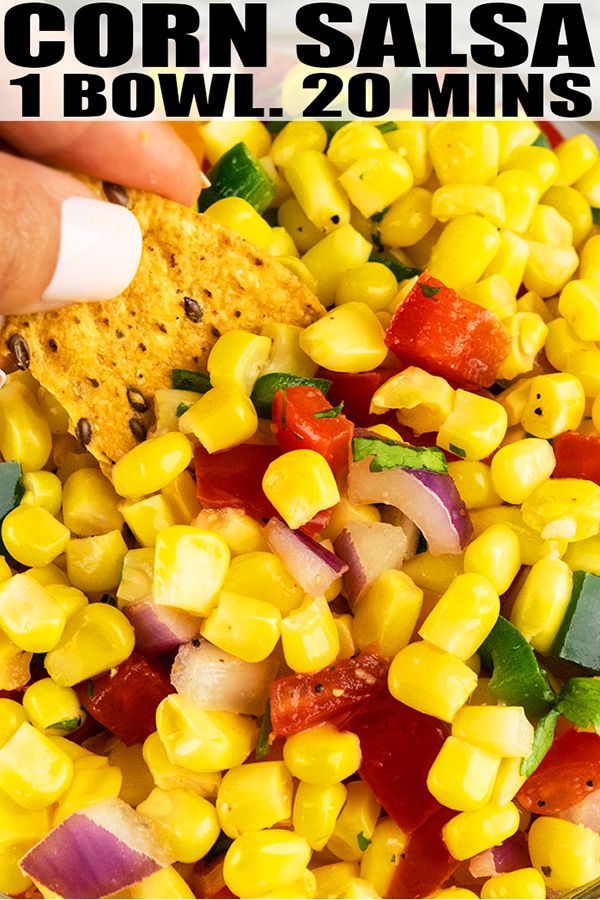 a person holding a tortilla chip over a corn salad