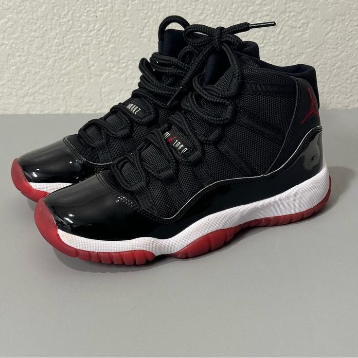 The Air Jordan 11 Retro Playoffs 2019 For Grade School (Gs) Uses The Classic Black/White/Varsity Red ‘Bred’ Colorway Introduced In 1996. The Patent Leather Mudguard, Nylon Mesh Upper, Tongue, Webbed Eyestays, And Rope-Like Laces Are Black. A White Nike Air Logo And Swoosh Appear On The Black Insole. The Black Leather Collar Features A Red-Stitched Jumpman And A White 23. A Black Jumpman Is Visible Through The Translucent Red Rubber Outsole With Spots Of Black Chevrons. A Carbon-Fiber Midfoot Sha Jordans 11 Black, Jordan 11 Black And Red, Cherry Red 11s, Red And Black Jordans, Jordans 11s, Air Jordans 11, Jordan 23 Shoes, Jordan 11 Red, Jordans Black And Red