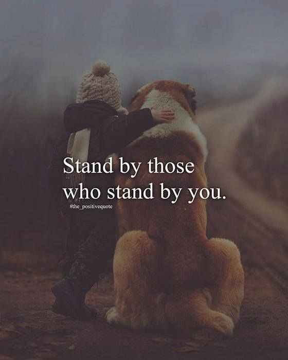 a teddy bear sitting on the ground with a person standing next to it that says, stand by those who stand by you