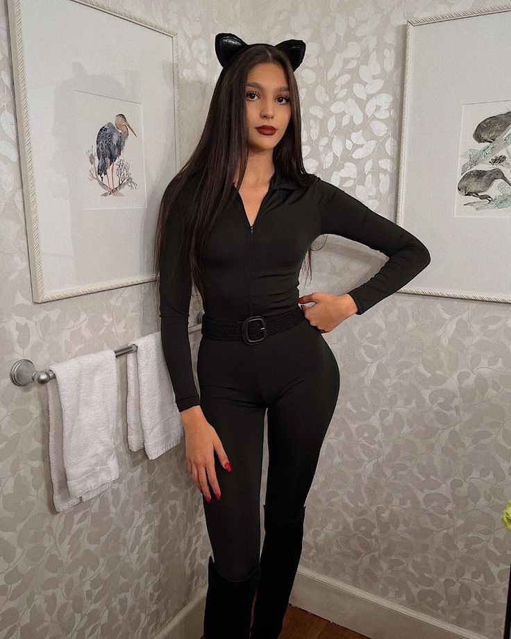 a woman in black catsuit standing next to a wall