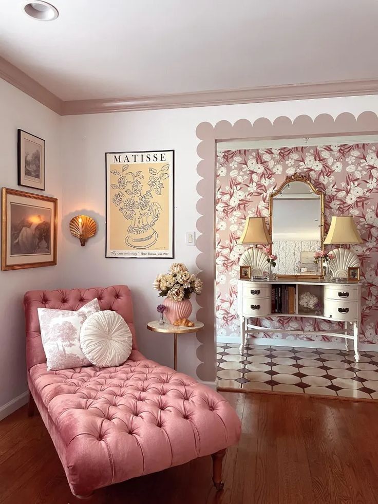 a pink chaise lounge chair sitting in front of a mirror and table with flowers on it