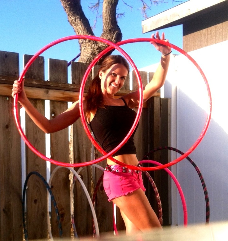 a woman in pink shorts and black shirt holding two large hoop rings over her head