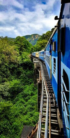 a blue train traveling down tracks next to lush green hillside covered in trees and bushes