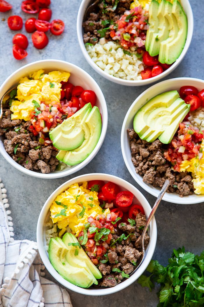 four bowls filled with meat, rice and veggies next to some cherry tomatoes