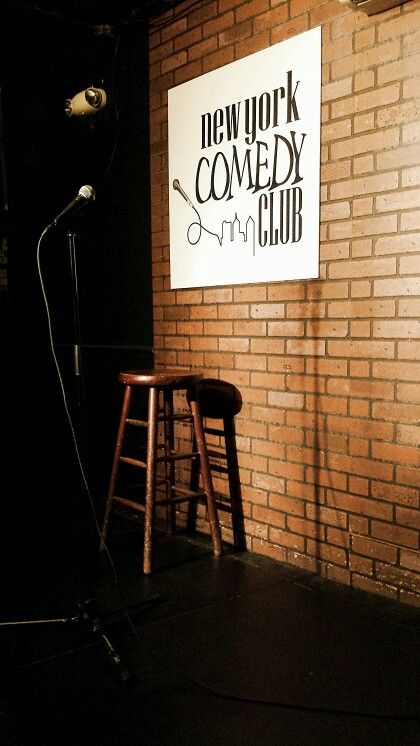 a brick wall with a sign that says new york comedy club on it and two stools