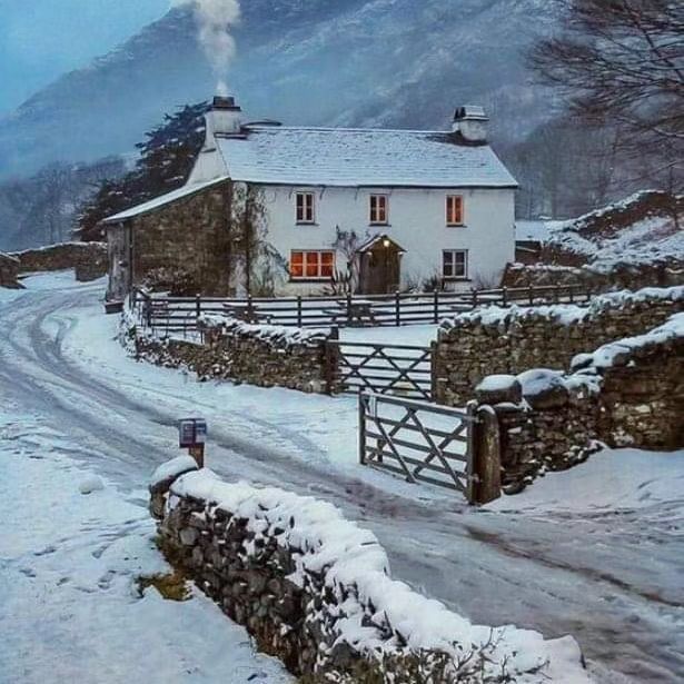 a white house sitting on the side of a snow covered road next to a stone wall