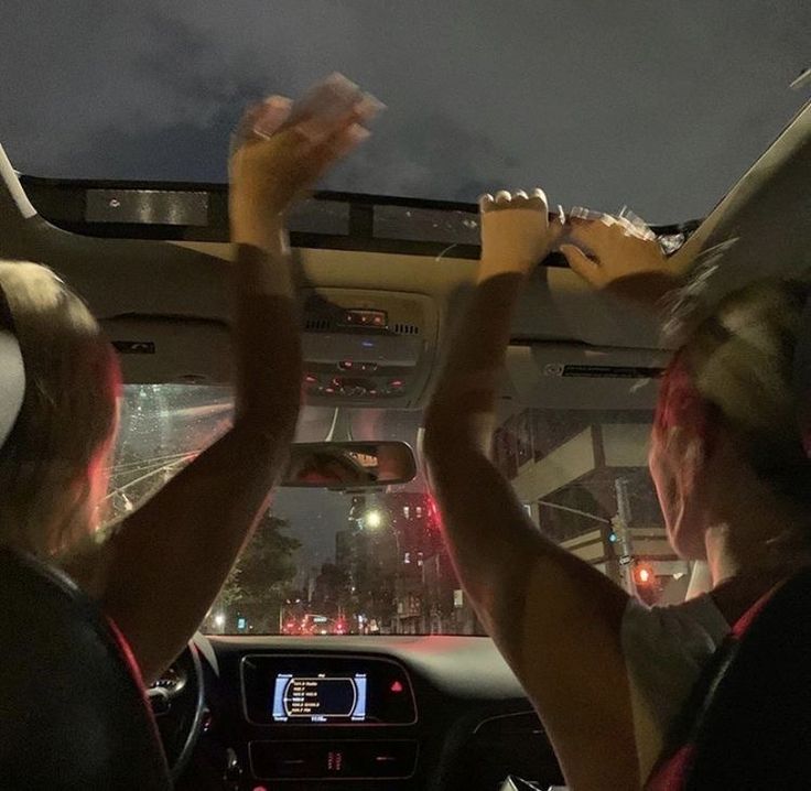 two people sitting in a car with their hands up and one person holding an object