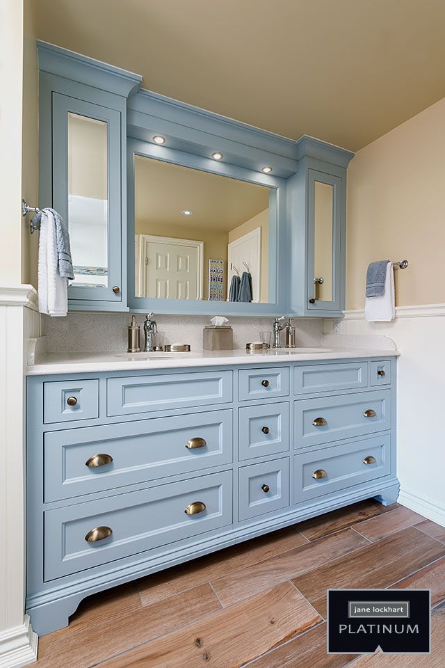 a bathroom with blue cabinets and white counter tops, wood flooring and a large mirror on the wall