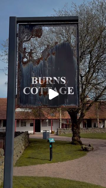 a sign that reads burns cottage in front of a building with trees and grass around it