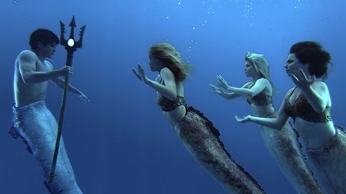 three mermaids are standing in the water with their backs to each other and one is holding a spear