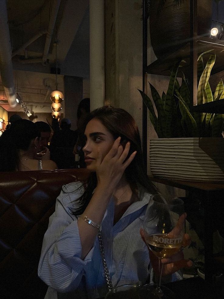 a woman sitting at a table with a glass of wine in her hand while talking on the phone