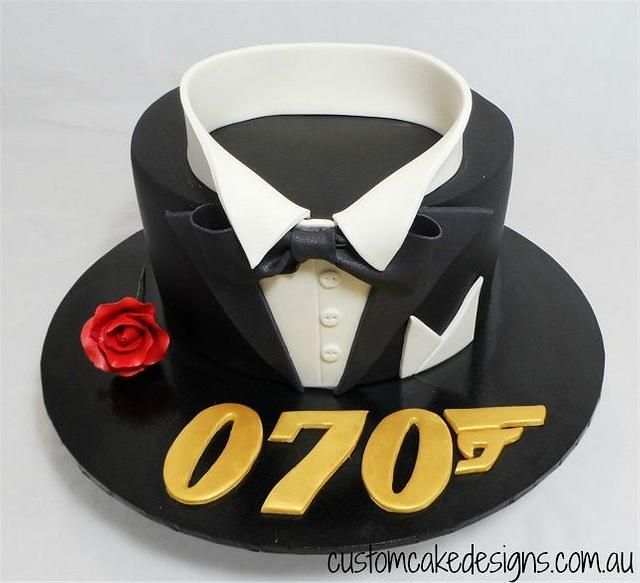 a black hat with gold letters and a red rose sits on top of the cake