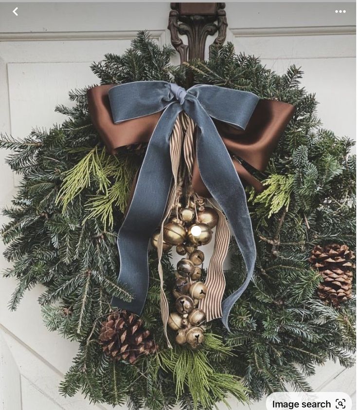 a christmas wreath with bells and pine cones hanging on the front door, decorated with blue ribbon