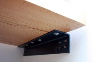 a wooden shelf with two black brackets on it's side and a white wall in the background