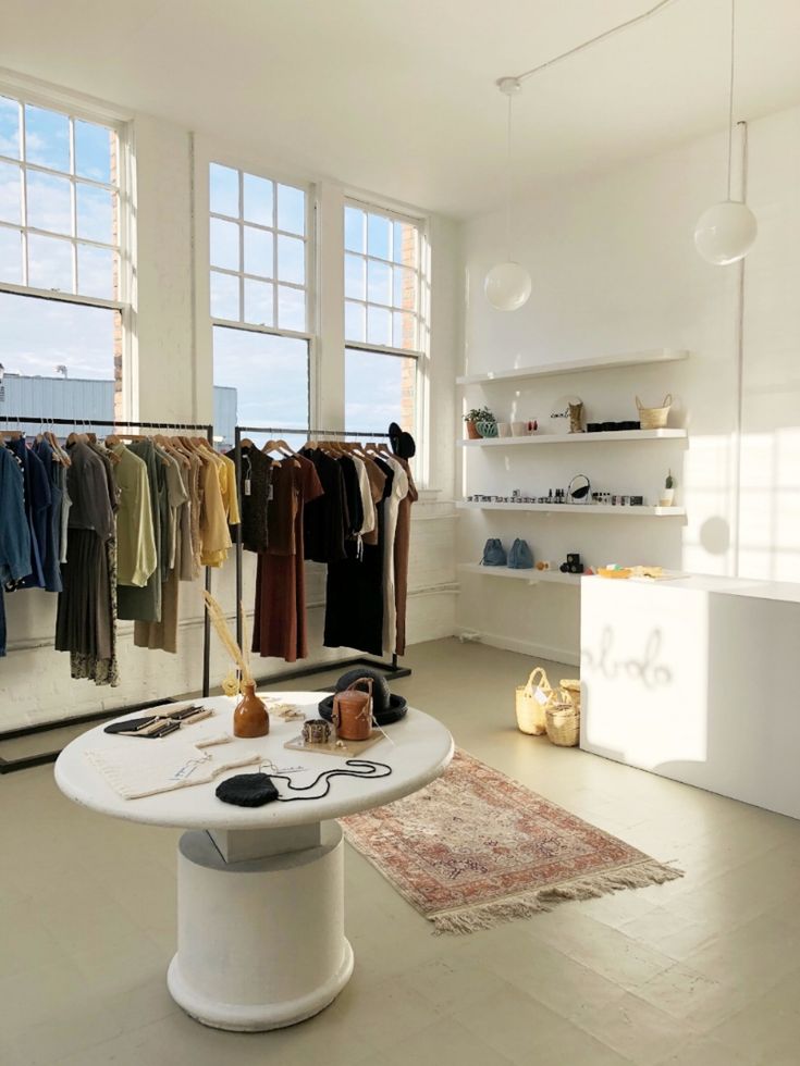 a room filled with lots of clothes on racks next to a table and chairs in front of large windows