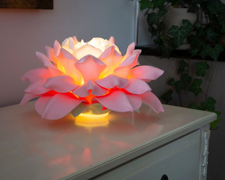 a lit up flower sitting on top of a white dresser